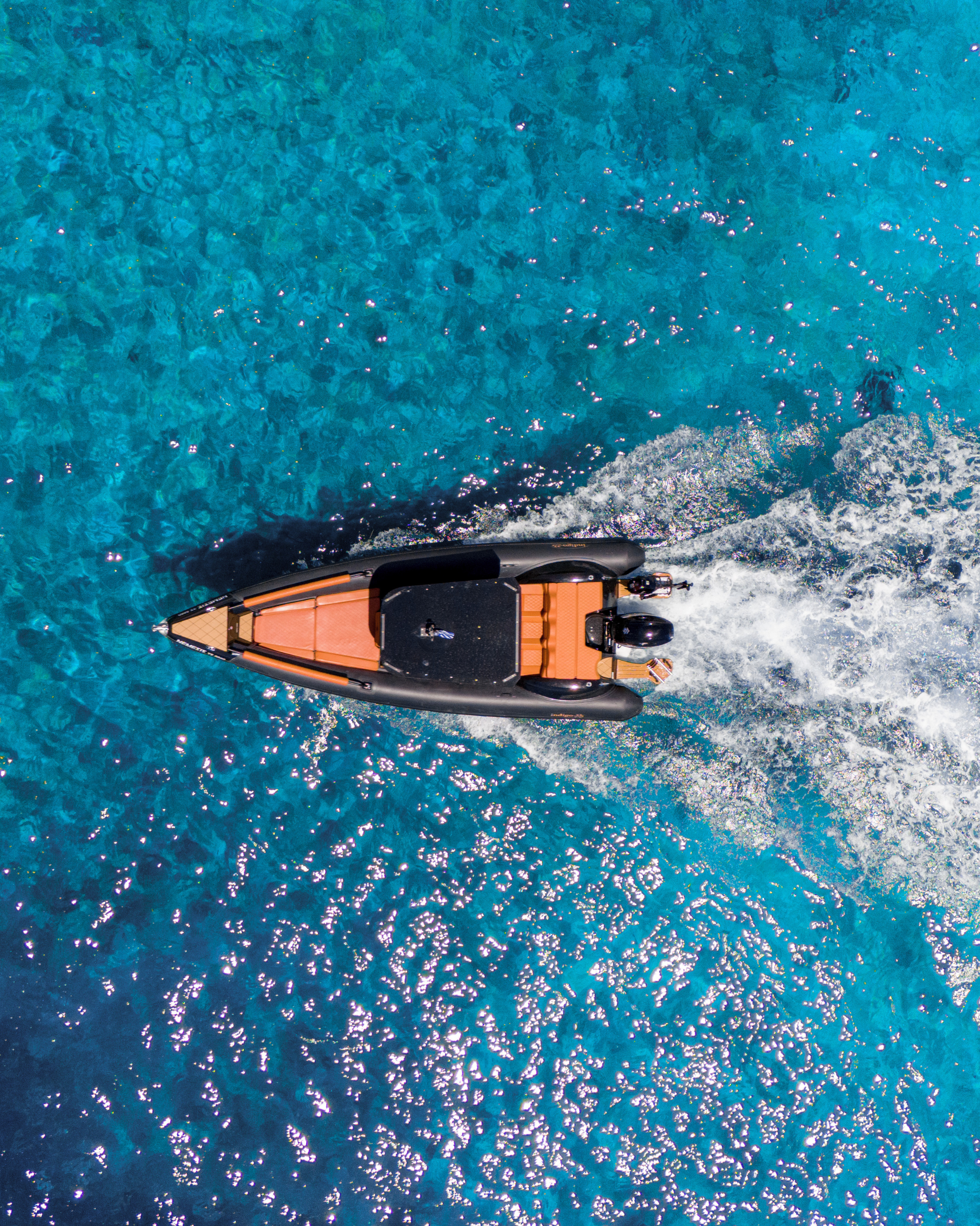 A speedboat cutting through clear blue water from an aerial perspective