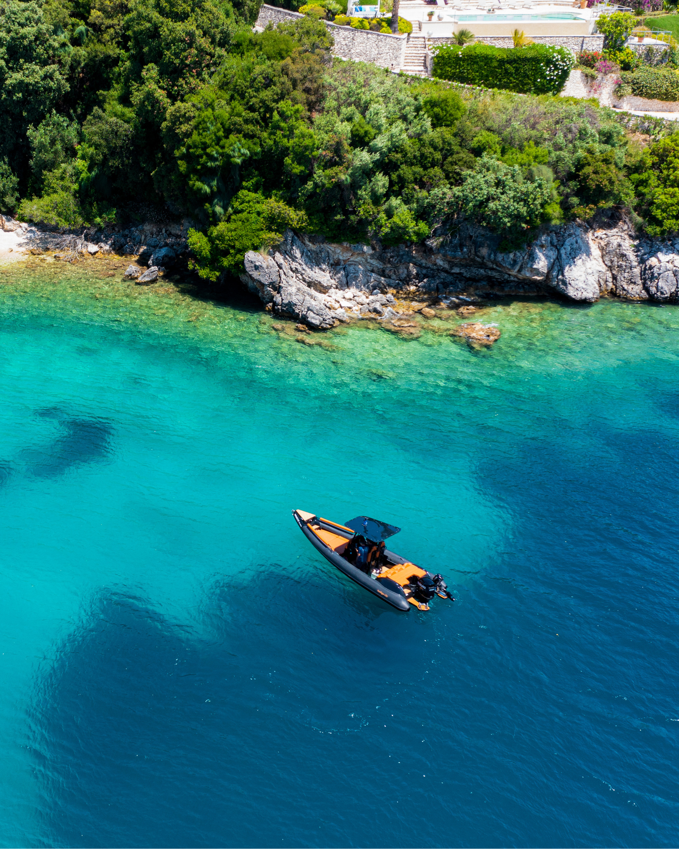 Boat in clear blue water near a rocky coastline with greenery | oasis premium corfu 