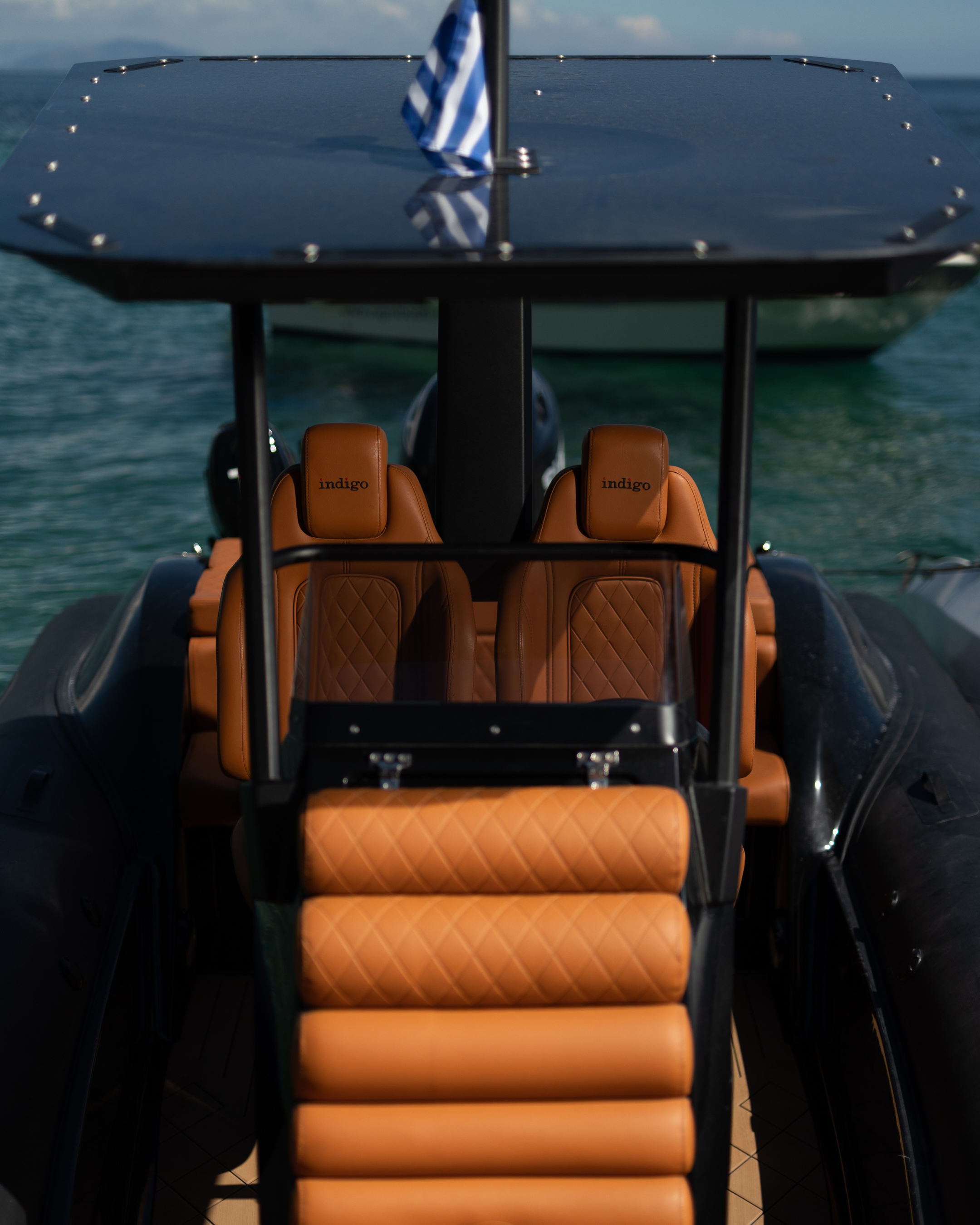 Luxury boat interior with brown leather seats and a Greek flag on a body of water.