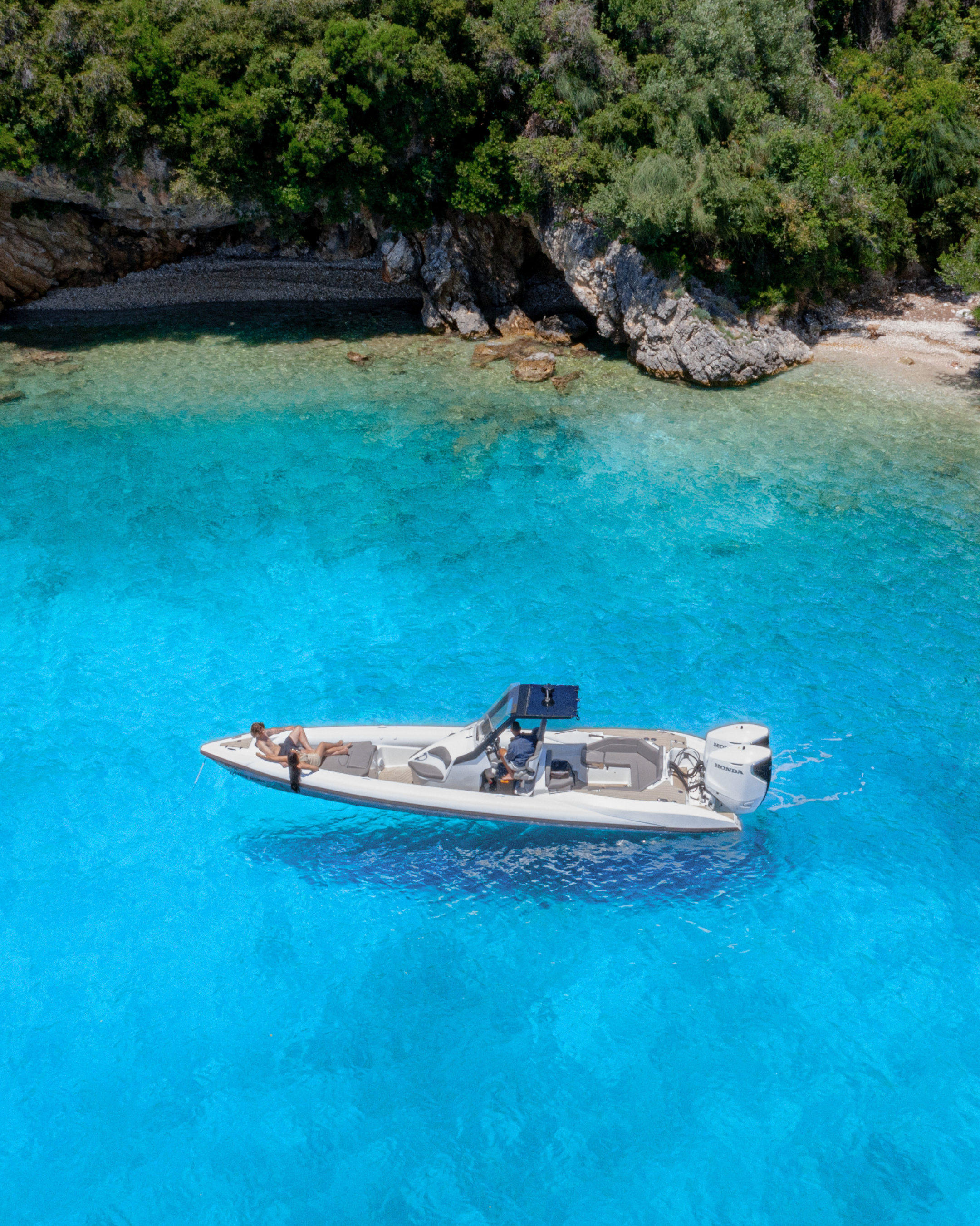 Boat floating in clear blue water with a rocky coastline in the background