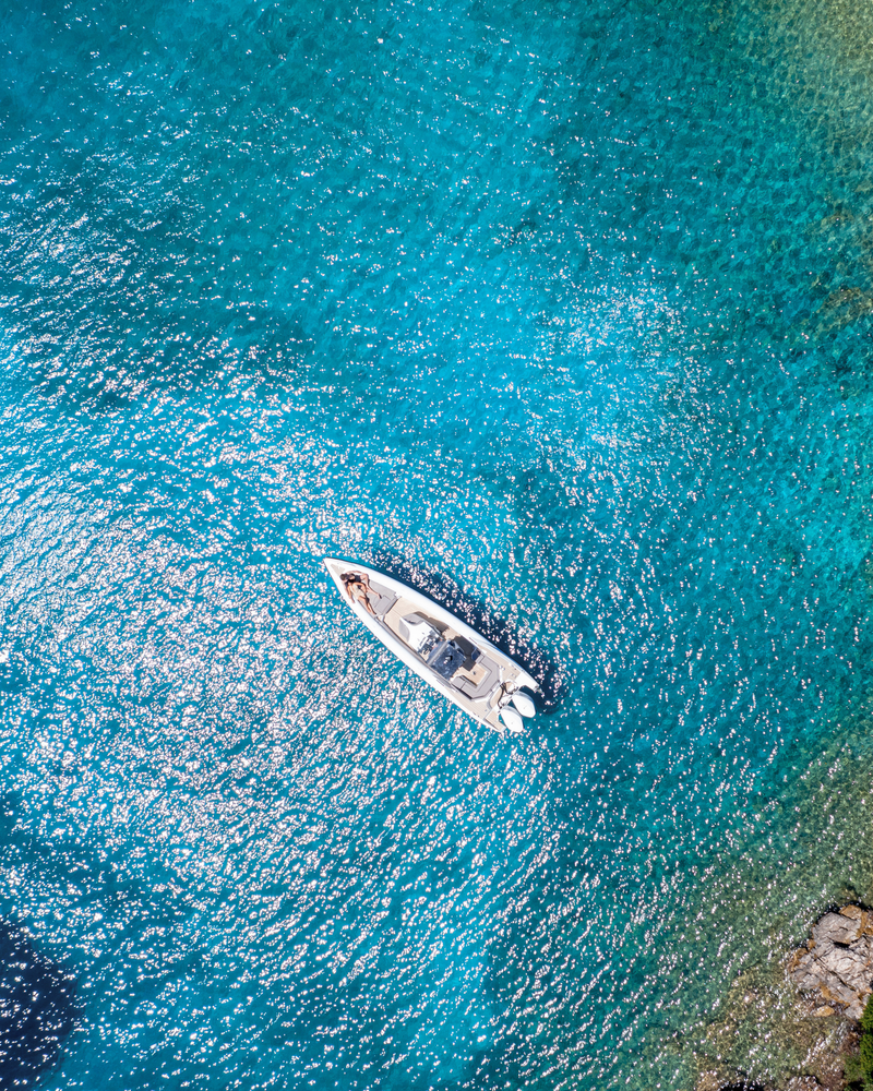 Aerial view of a boat on clear blue water with sunlight reflections.
